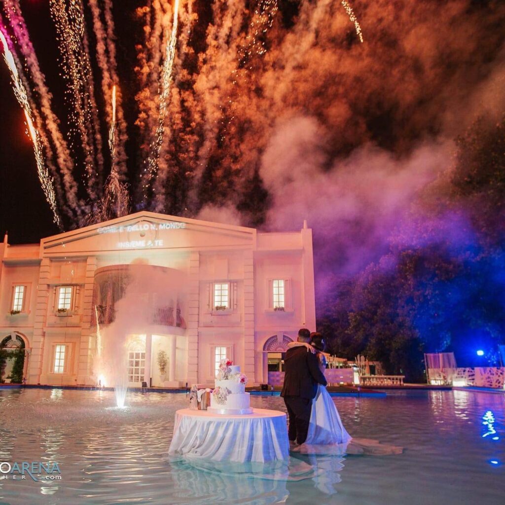 Sposi al taglio della torta in piscina con fuochi d’artificio sulla villa