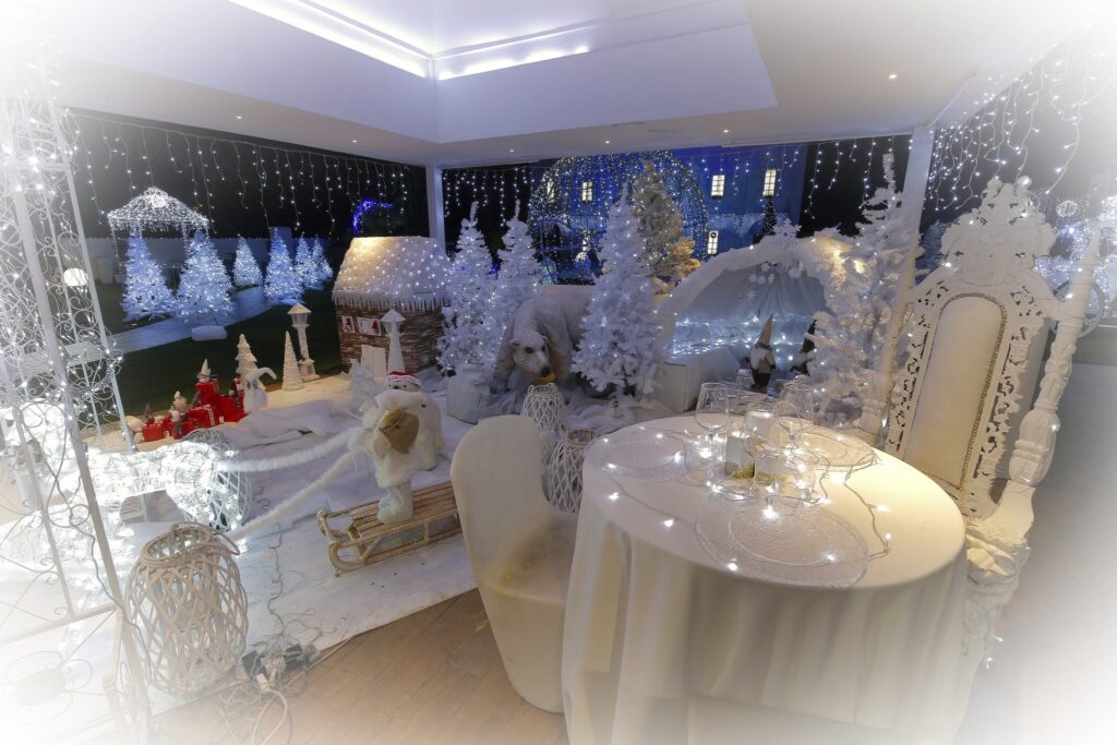 Scenografia natalizia bianca con poltrona, alberi e decorazioni illuminate a Villa ReNoir
